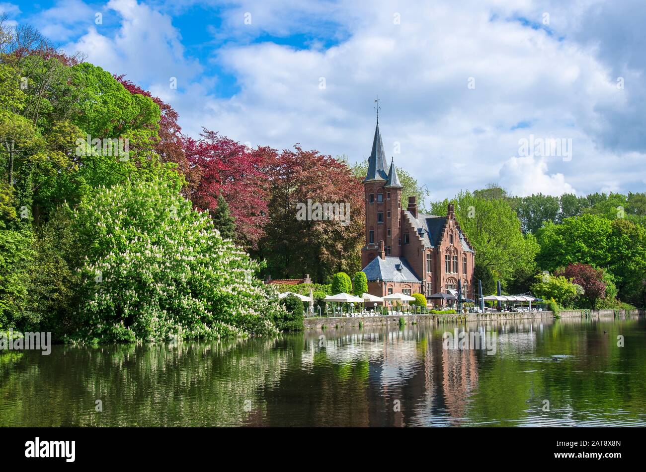 Vista sul tranquillo spazio verde pubblico con il lago Minnewater e il piccolo castello di Bruges durante la giornata di sole in primavera, in Belgio Foto Stock