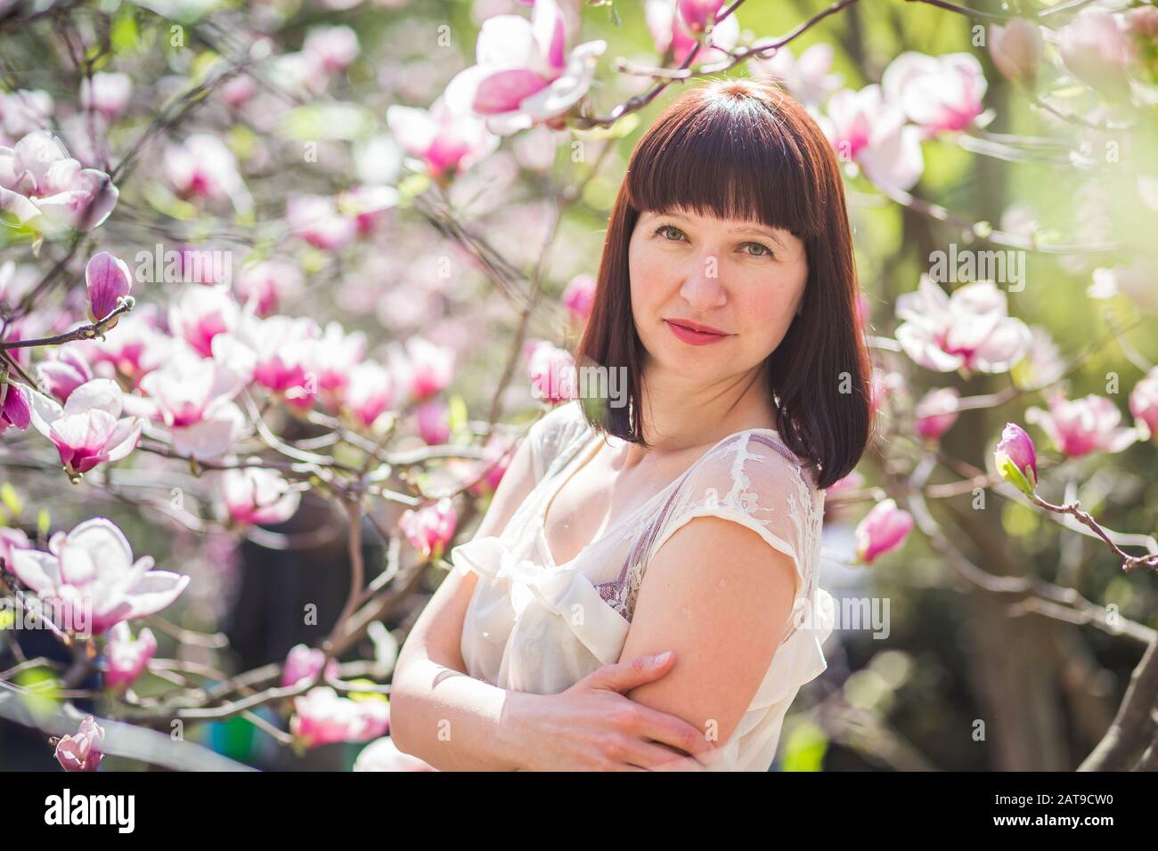 Bella dai capelli scuri donna tra i rami della magnolia. primi fiori in alberi in primavera. Foto Stock