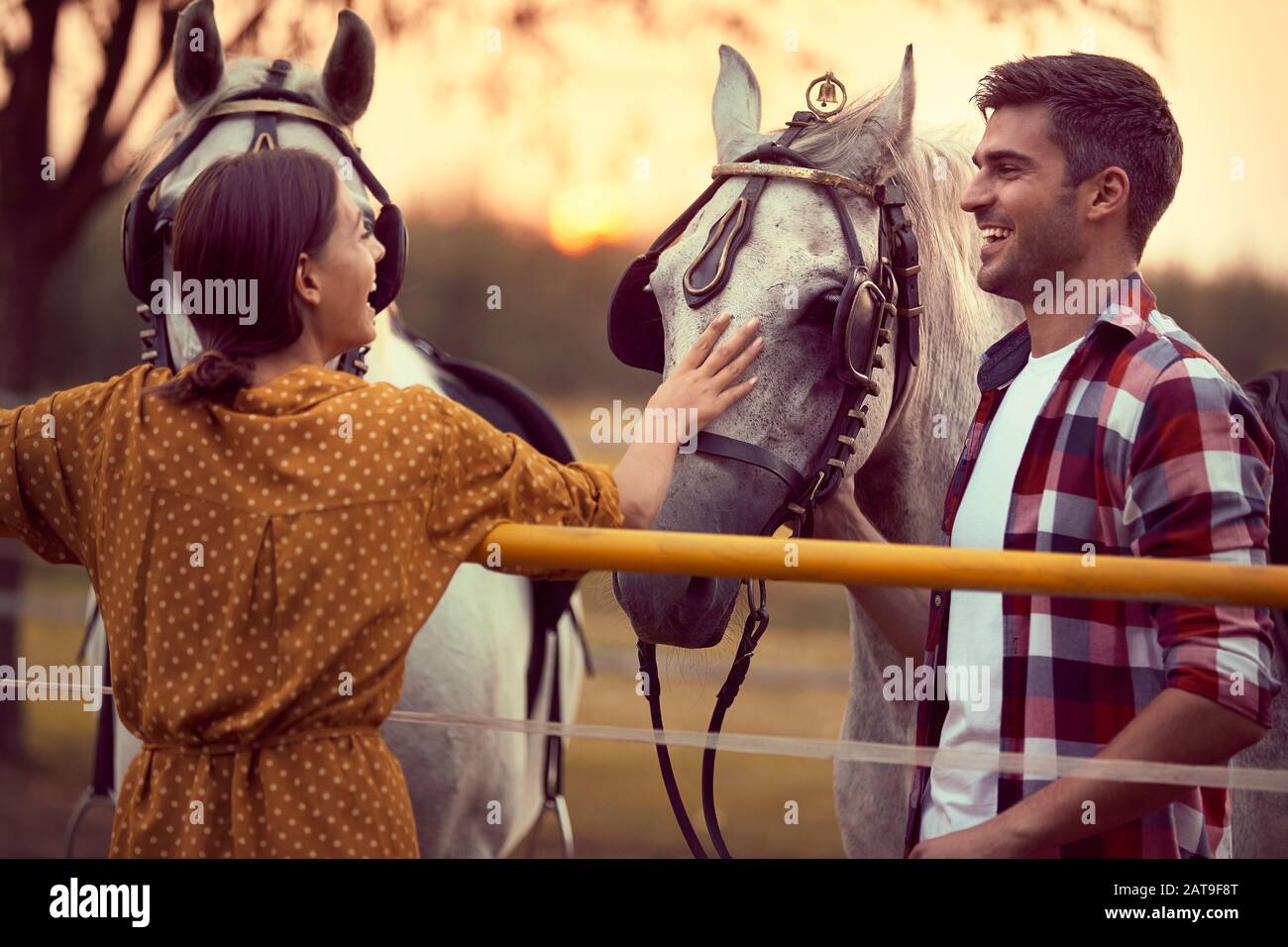 Coppia felice di divertirsi sul ranch cavallo, persone innamorate. Divertimento in campagna, ora d'oro del tramonto. Libertà natura concetto. Foto Stock