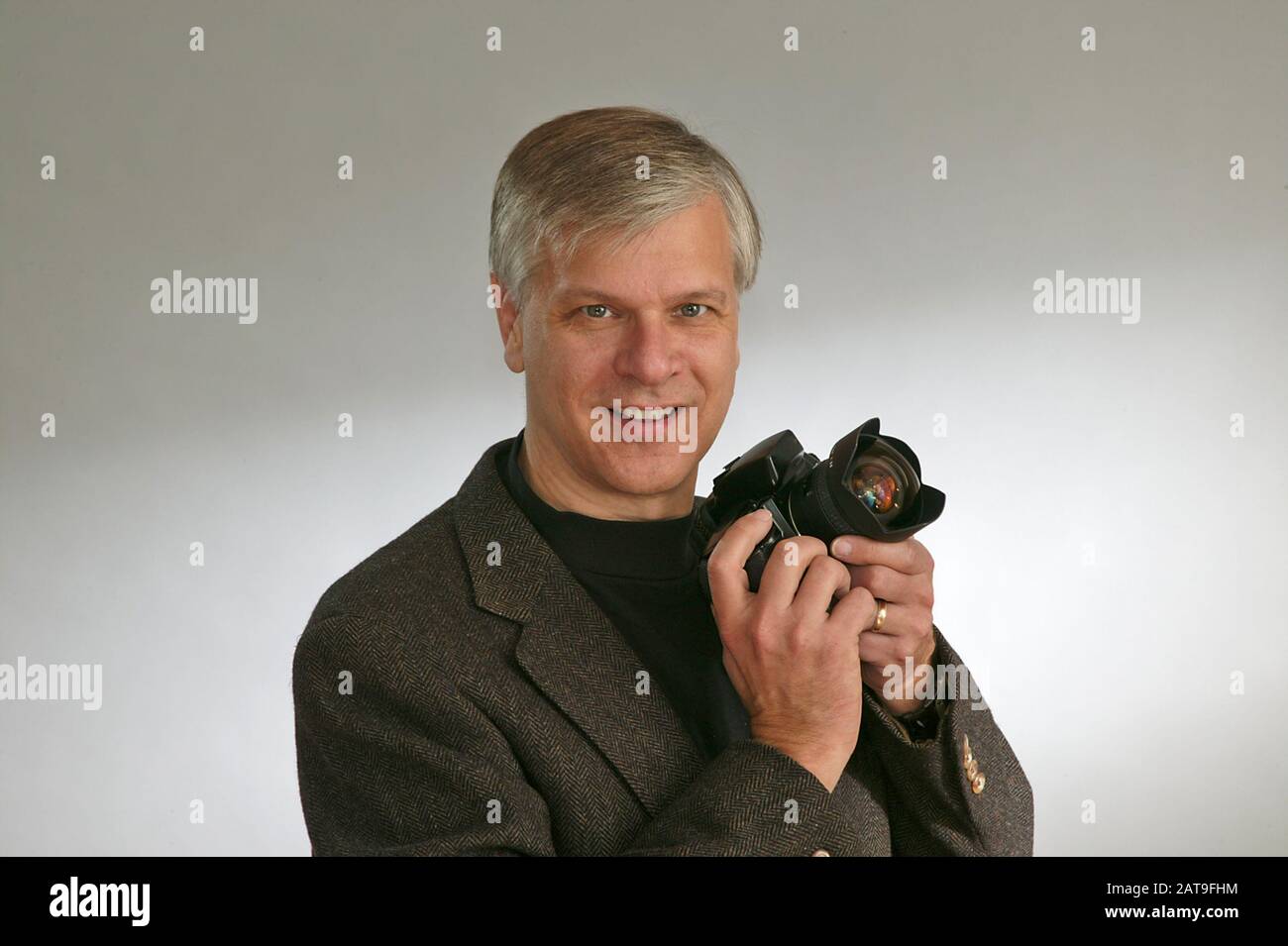 Fotografo con sorriso che tiene la fotocamera reflex. Foto Stock