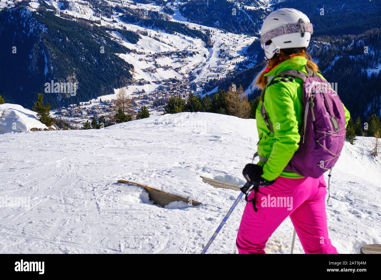 Ragazza sciatore che si affaccia verso il villaggio di Corvara nelle Dolomiti italiane, da una pista da sci sopra la città di montagna. Inverno sci vacanze concep Foto Stock