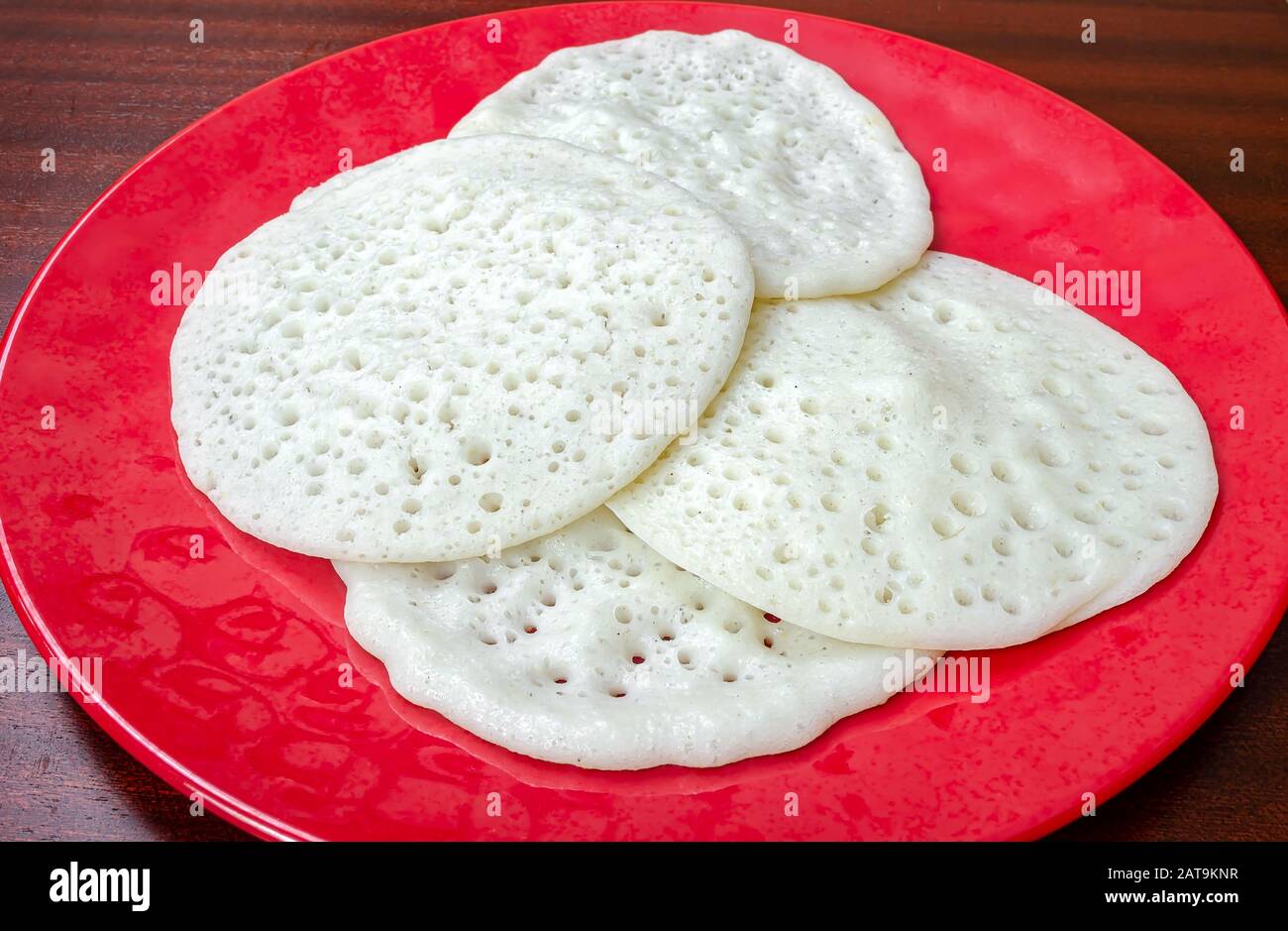 Kerala Appams speciali in un piatto rosso su un tavolo di legno pronto per essere mangiato. Foto Stock