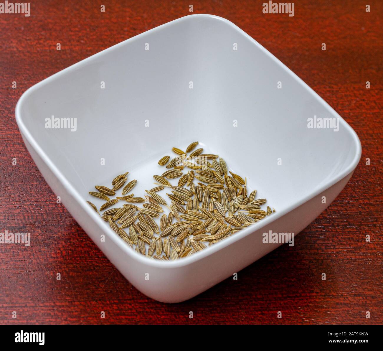 Macro shot di semi di cumino in una ciotola bianca su un tavolo di legno Foto Stock