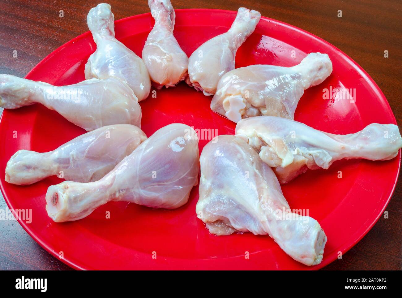 Un mazzetto di pezzi di pollo crudi in una piastra rossa, pronti per la frittura. Foto Stock