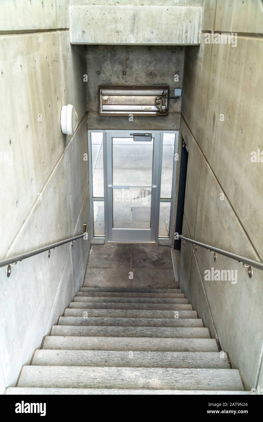 Scala all'interno di un edificio che scende fino ad una porta di vetro che porta all'esterno Foto Stock