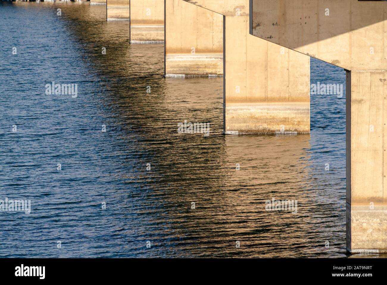 Vista sotto un ponte a trave con abutment contro l'acqua del lago illuminata dal sole Foto Stock