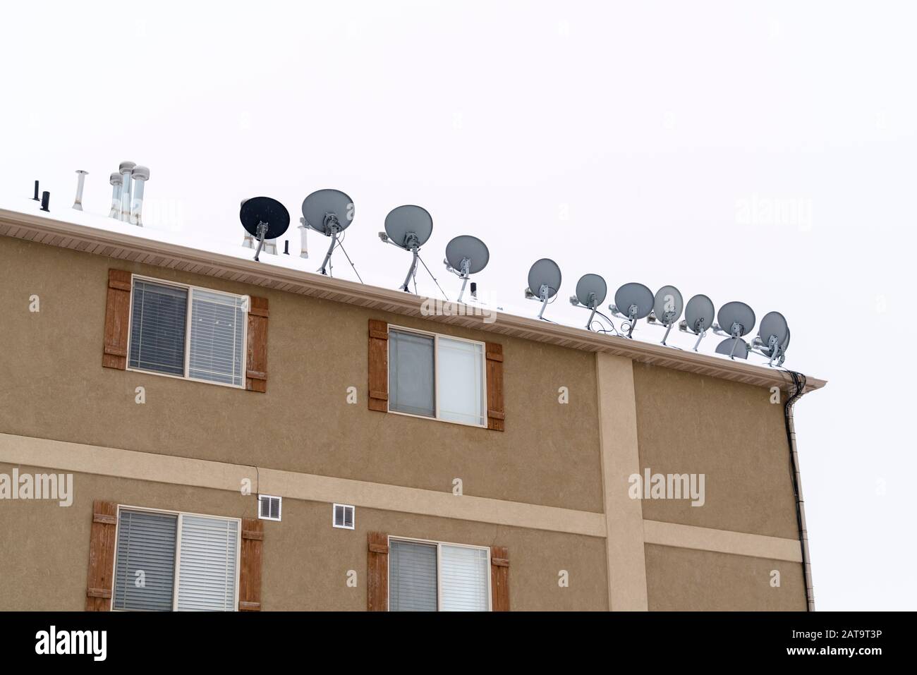 Antenne a forma di ciotola montate sul tetto innevato dell'edificio residenziale in inverno Foto Stock