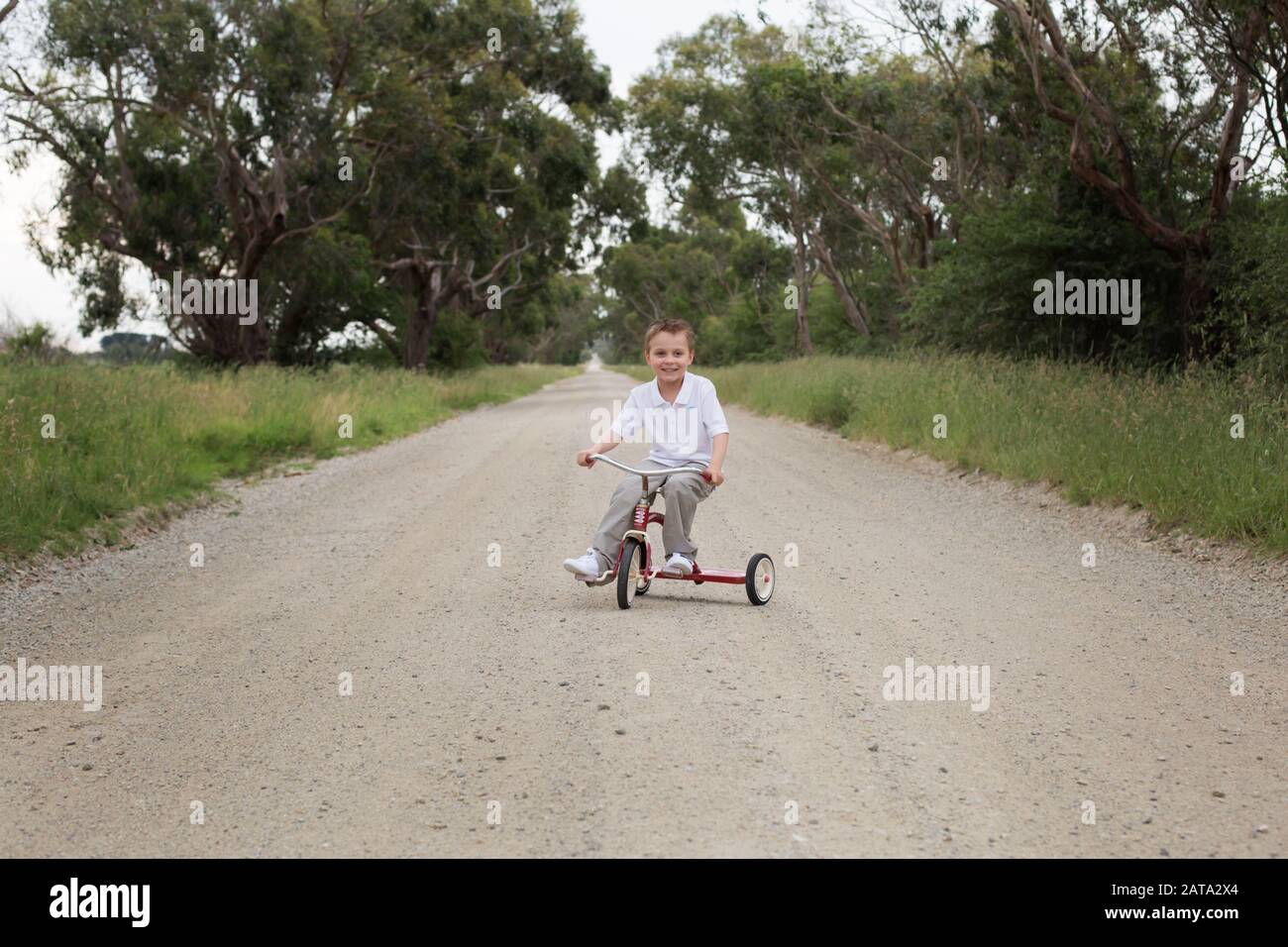 Un ragazzo australiano caucasico che cavalcava un triciclo rosso su una strada sterrata nel paese Foto Stock