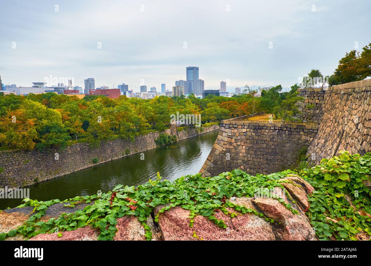 La vista lungo il fossato Interno del Castello di Osaka con lo skyline di Osaka sullo sfondo. Osaka. Giappone Foto Stock