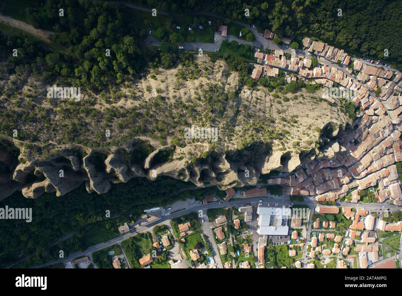 VISTA VERTICALE AEREA. Villaggio provenzale ai piedi di una formazione rocciosa stranamente sagomata. Les Mées, Provenza, Francia. Foto Stock