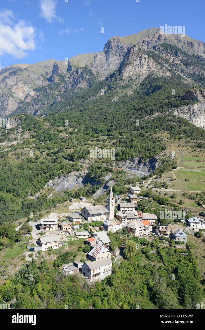 VISTA AEREA. Piccolo villaggio ai piedi di una montagna maestosa. Saint-Marcelin, Hautes-Alpes, Francia. Foto Stock