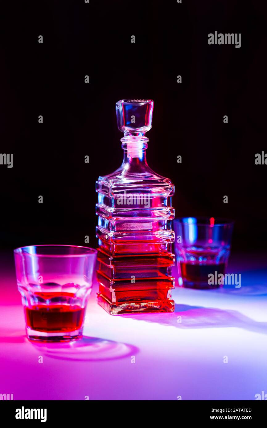 Caraffa quadrata in vetro con liquore con due bicchieri di vetro su tavolo bianco e sfondo nero. Foto Stock