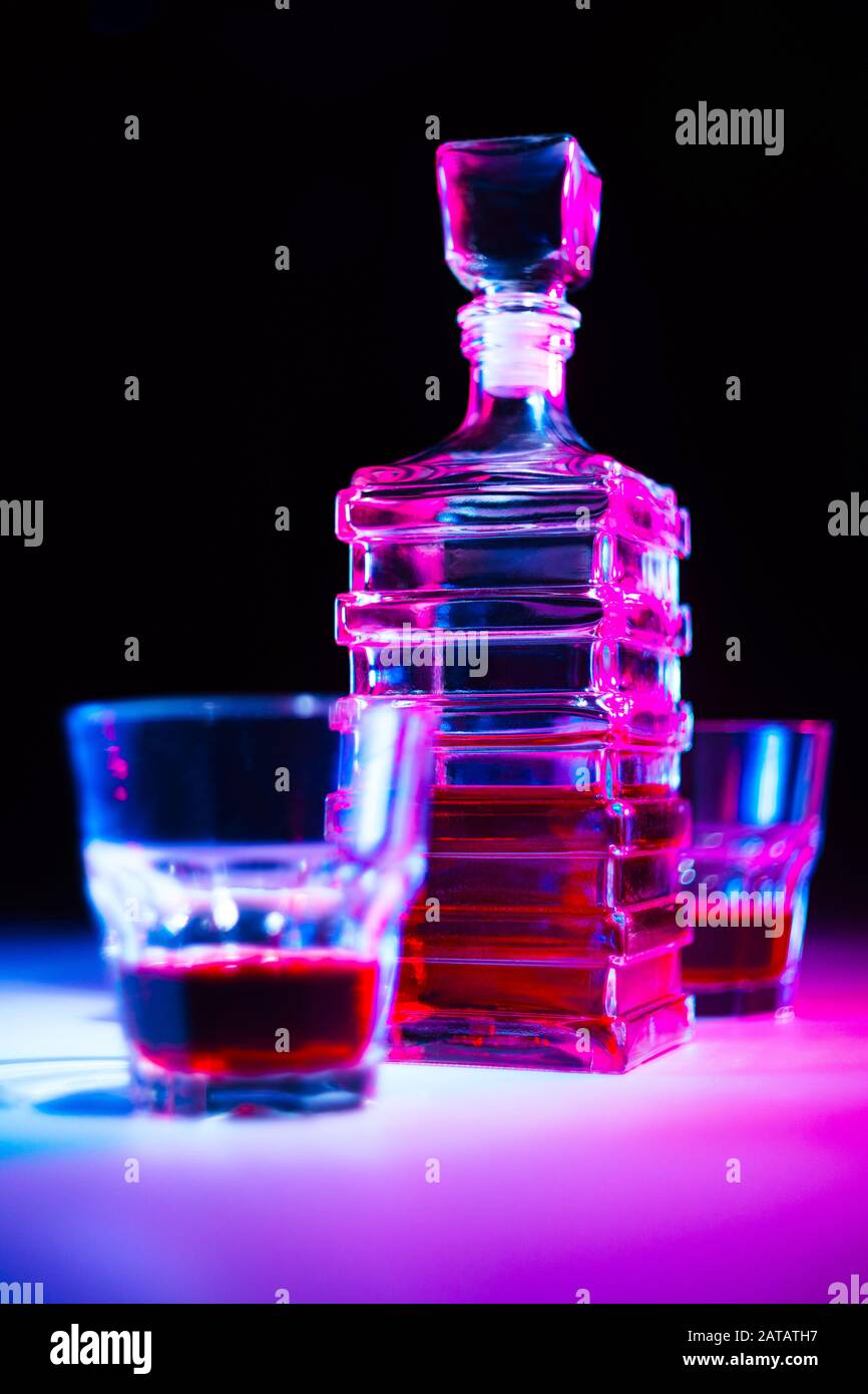 Caraffa quadrata in vetro con liquore con due bicchieri di vetro su tavolo bianco e sfondo nero. Foto Stock