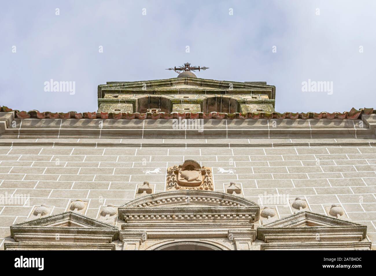 Campanile di una chiesa con una croce di metallo in cima e dettagli scolpiti in pietra sulla facciata, a ovest della Spagna, a Serradilla (Caceres) Foto Stock