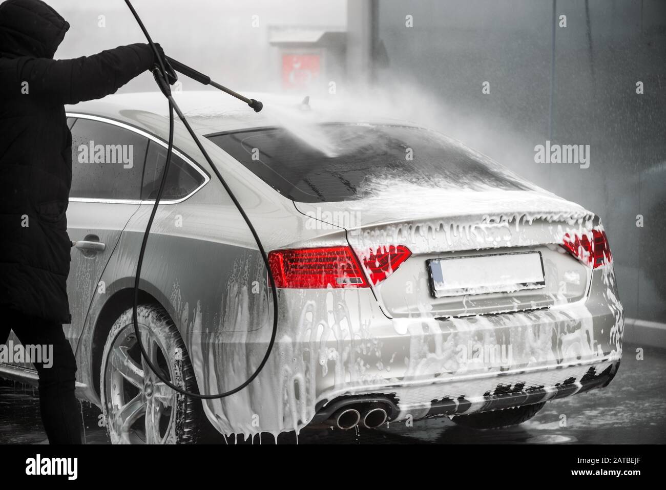 L'uomo lava la sua auto grigia sotto acqua ad alta pressione all'aperto. - Vista posteriore Foto Stock