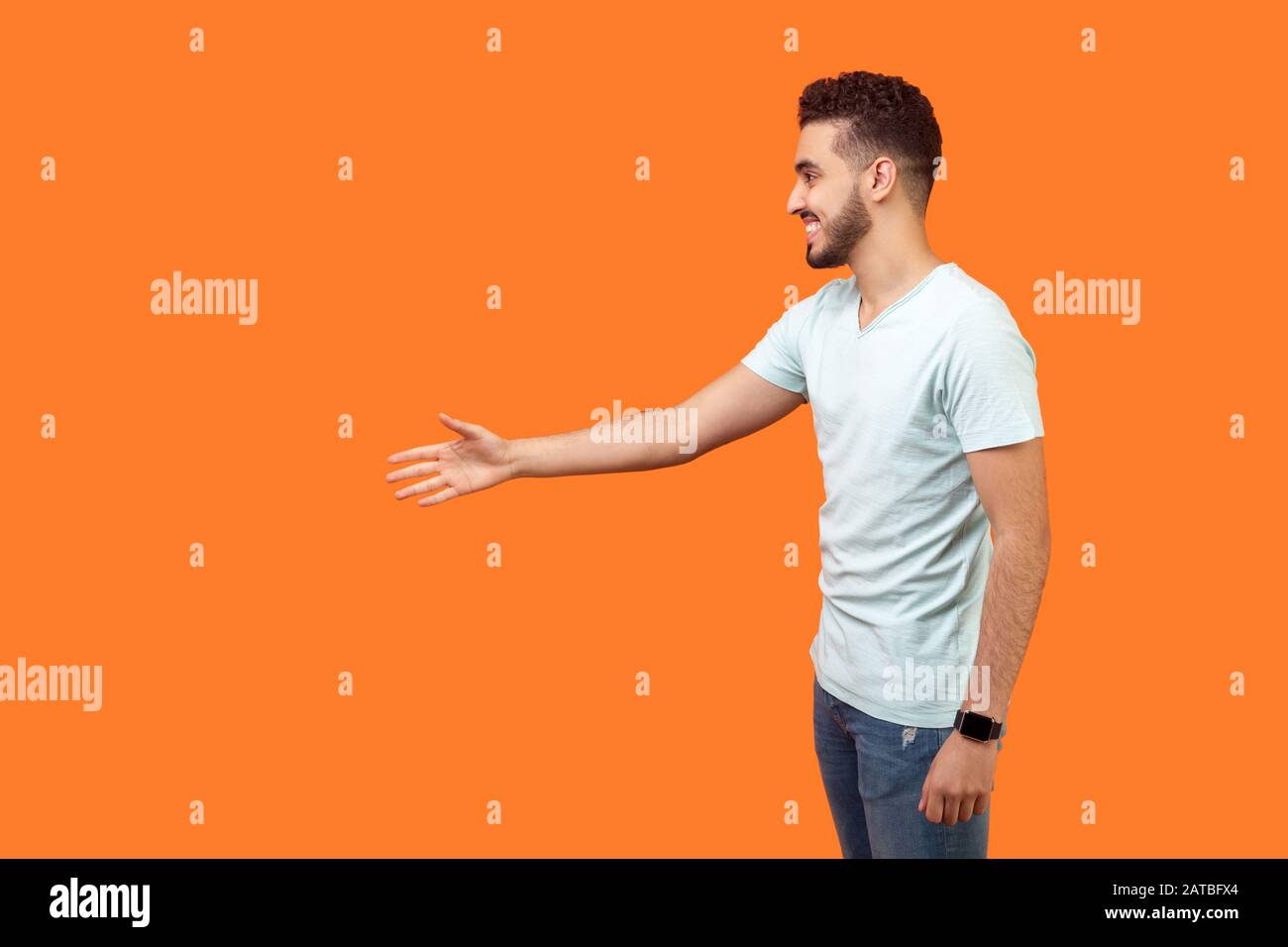 Ritratto con vista laterale di un amico positivo con barba in t-shirt bianca che dà mano a mano e saluto, vuoto spazio copia a sinistra per il testo. Indo Foto Stock