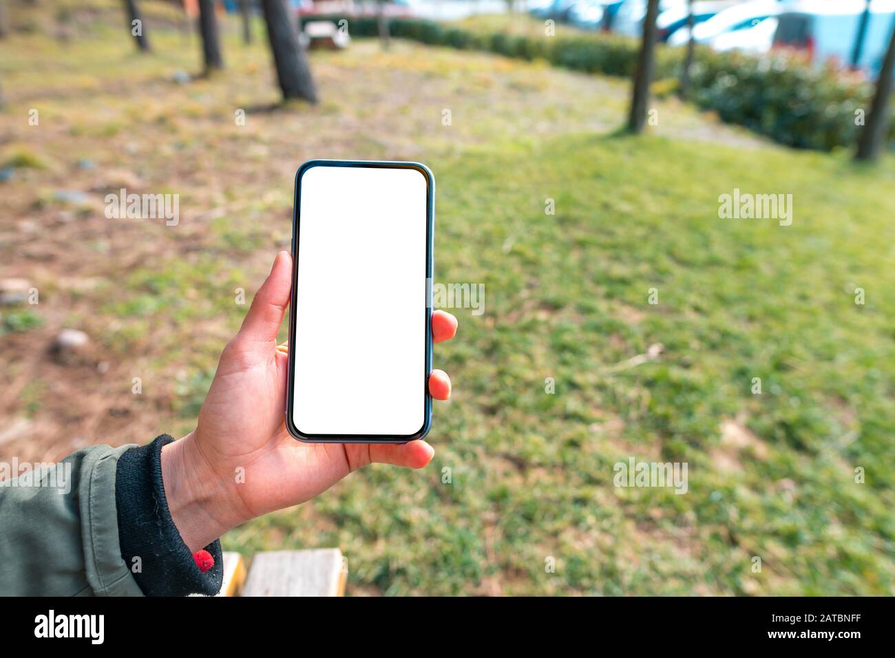 Immagine mockup dello smartphone con modello bianco schermo vuoto, mano donna tenuta e mostra mobile in natura all'aperto. Foto Stock