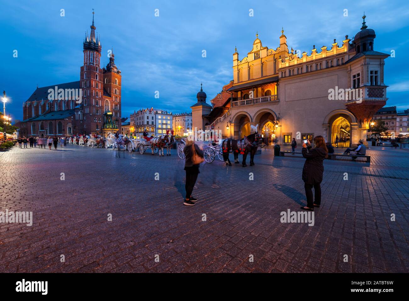 Cracovia, Polonia - 23 settembre 2018: Persone e fila di carrozze a cavallo nella piazza principale della città vecchia, centro storico al crepuscolo serale con S. Foto Stock