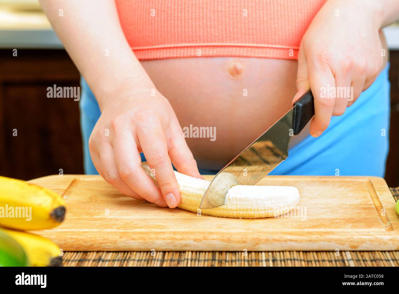 Donna incinta prepara una banana in cucina Foto Stock