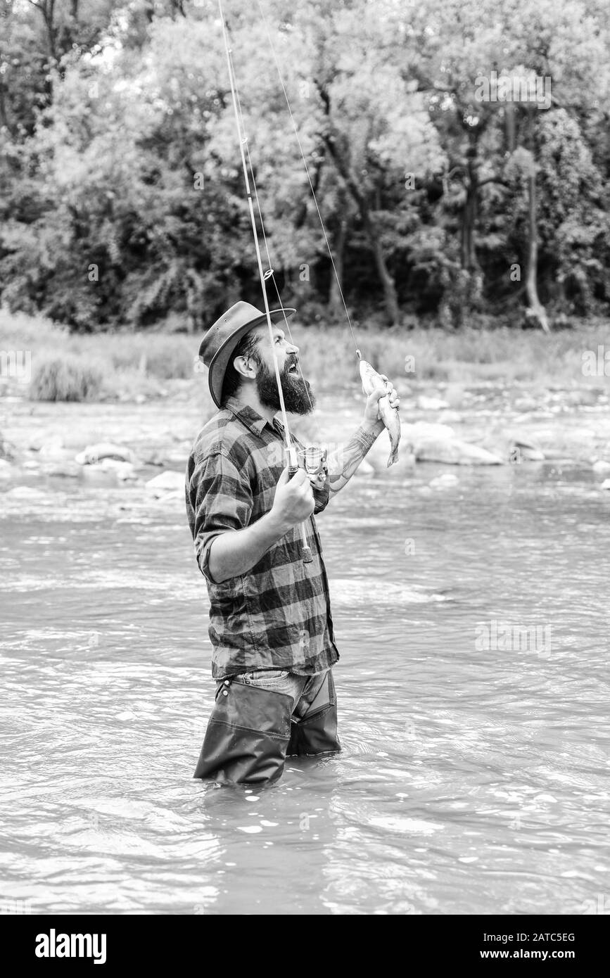 Uomo brutale indossare stivali di gomma riposare in acqua di fiume.  Attività del fine settimana. Pesca hobby maschile. La pesca richiede di  essere consapevoli e pienamente presente in questo momento. Fisher di