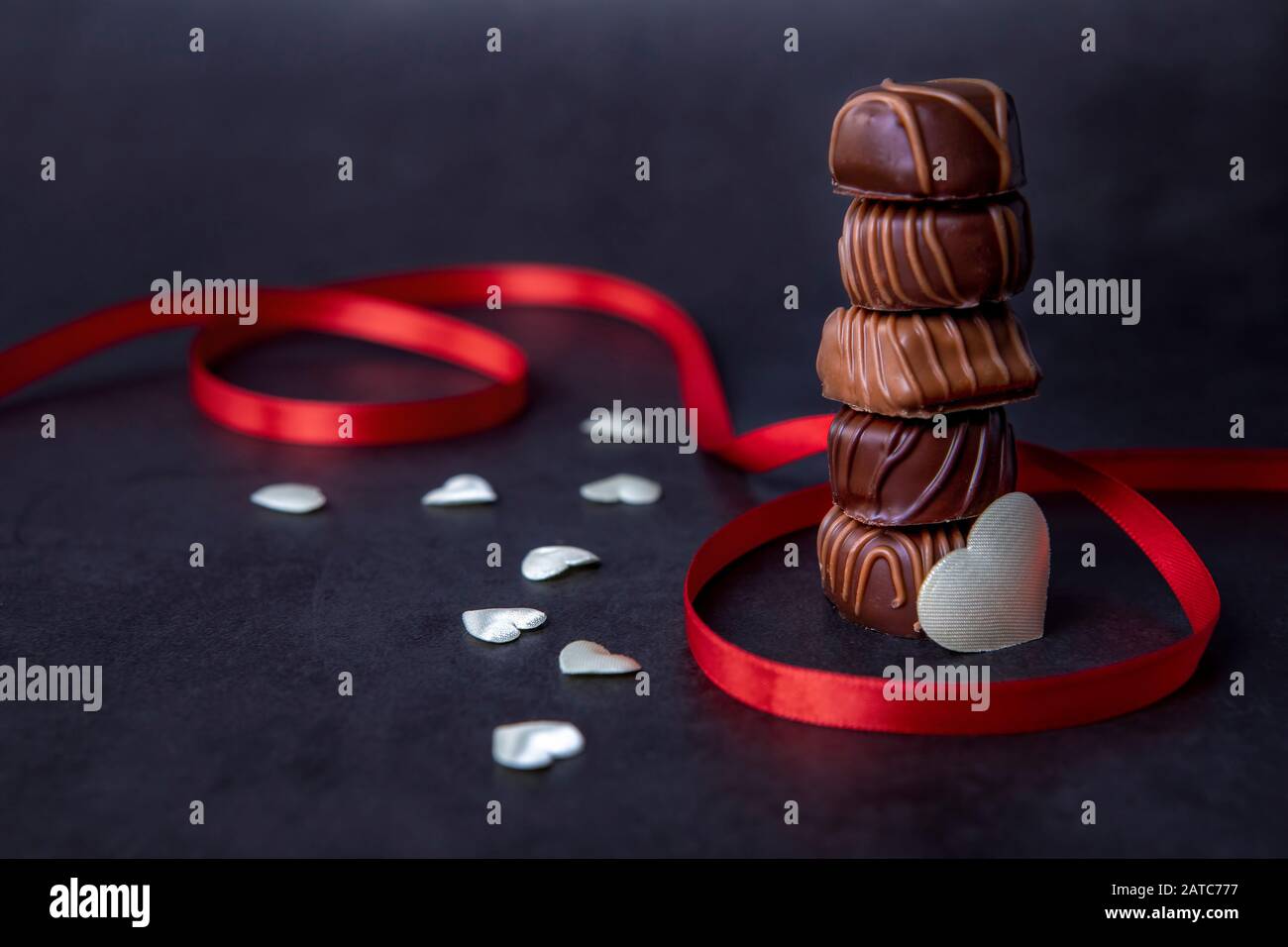 Pila di caramelle al cioccolato e nastro rosso su sfondo nero. Focus sul cioccolato. Foto Stock