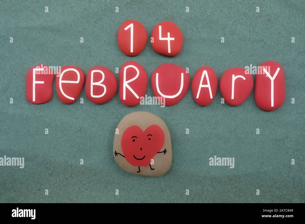 14 febbraio, San Valentino composto con lettere di pietra rossa e un cuore divertente su sabbia verde Foto Stock