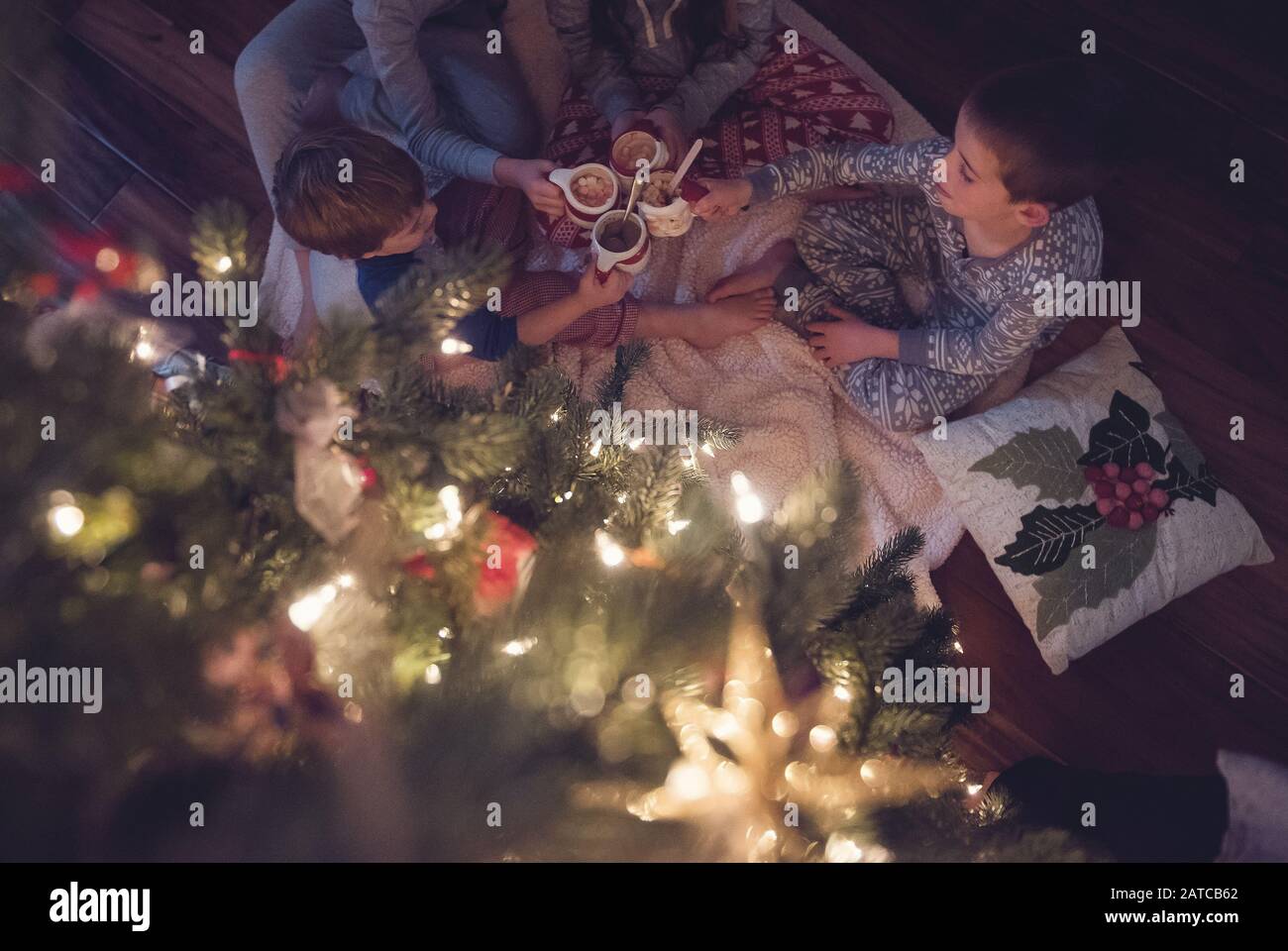 Quattro bambini seduti da un albero di Natale che bevono cioccolata calda con marshmallows Foto Stock