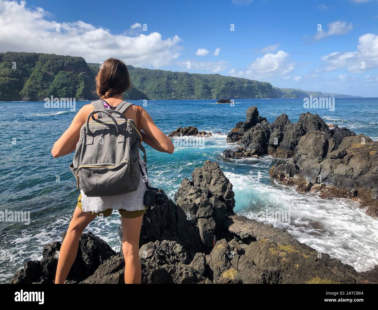 Donna che si erge sulle scogliere lungo Road to Hana guardando vista, Maui, Hawaii, USA Foto Stock