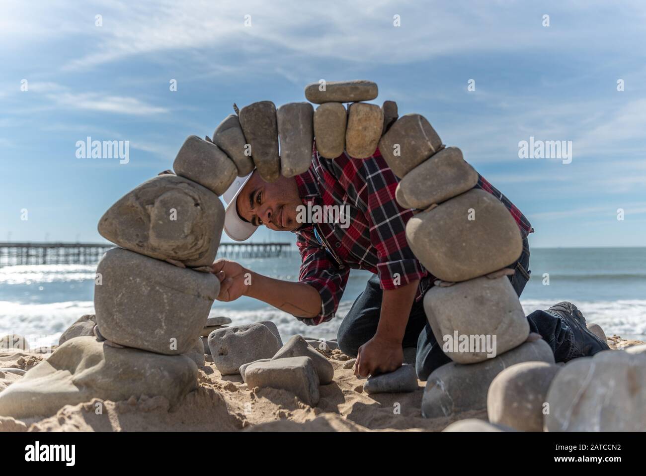 Juan Manuel Cisneros guarda attraverso l'apertura di pietra, mentre la costruzione dell'arco ingegnerizzato da roccia del fiume sulla spiaggia di Ventura il 30 gennaio 2020 i Foto Stock
