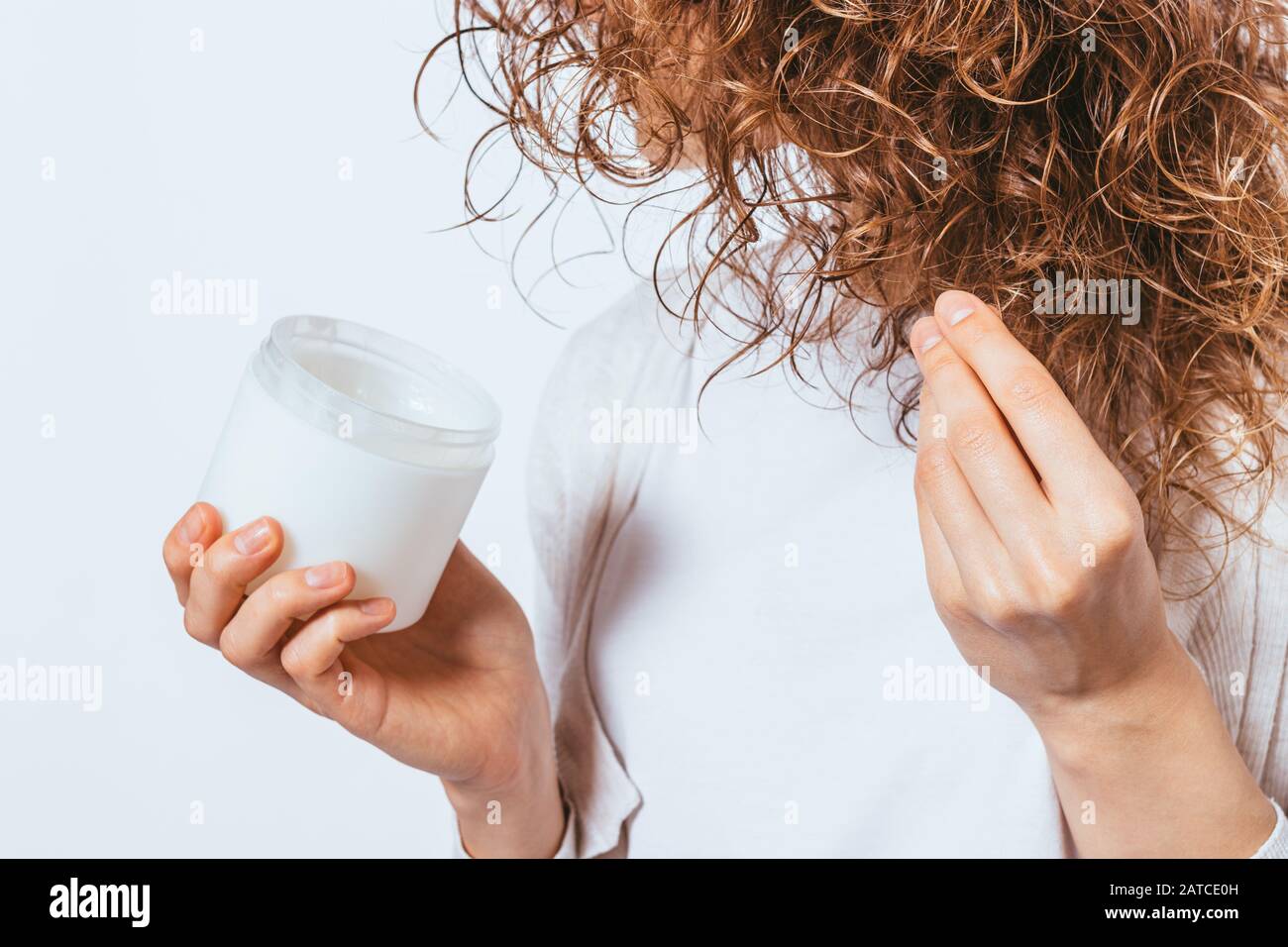 Le mani femminili applicano l'olio di cocco cosmetico sulle sue punte arricciate dei capelli, primo piano. Foto Stock