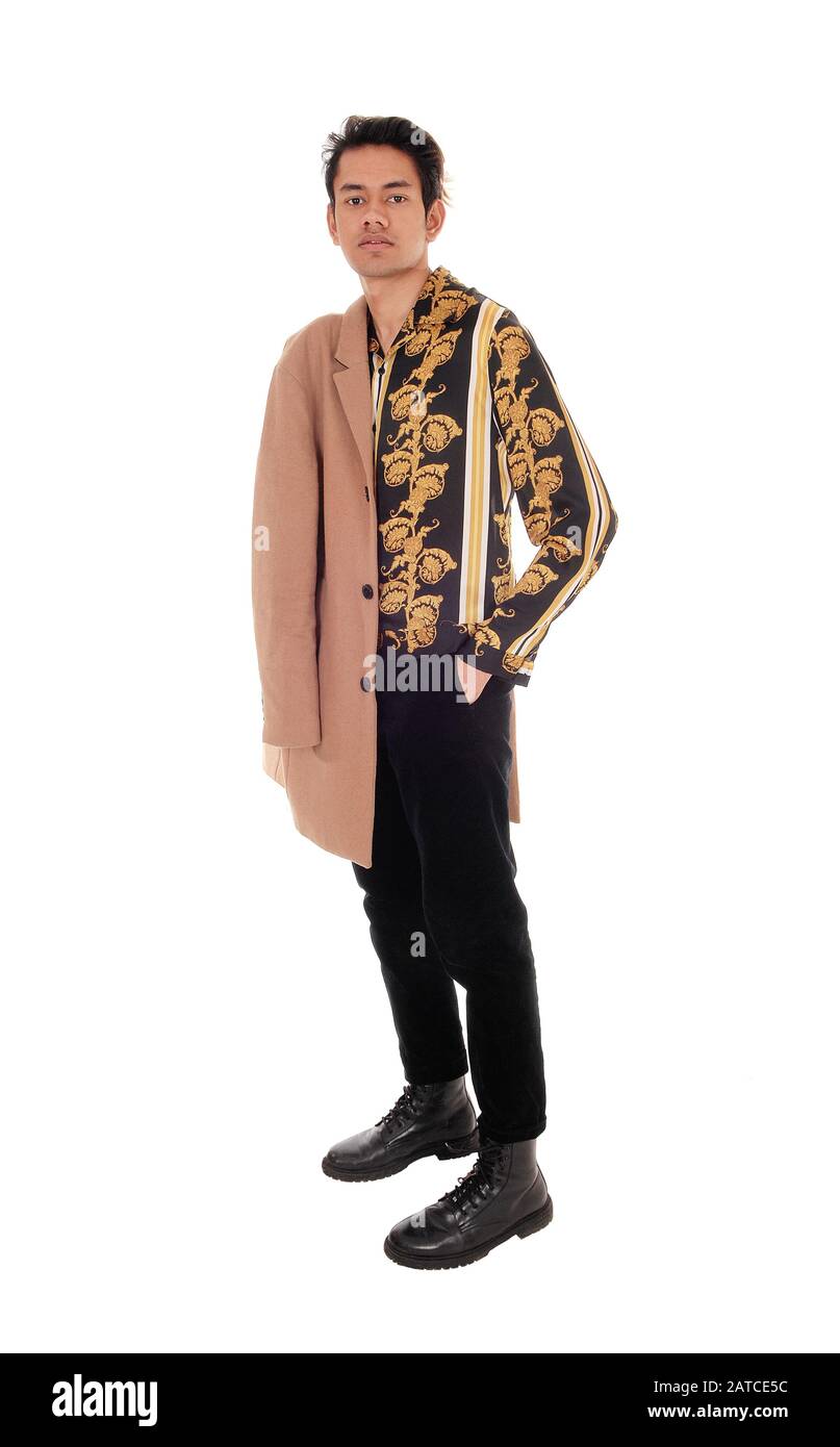 Un giovane alto skinny in una camicia dorata stampata e la sua mano in tasca, con un cappotto beige sopra la spalla, isolato per sfondo bianco Foto Stock