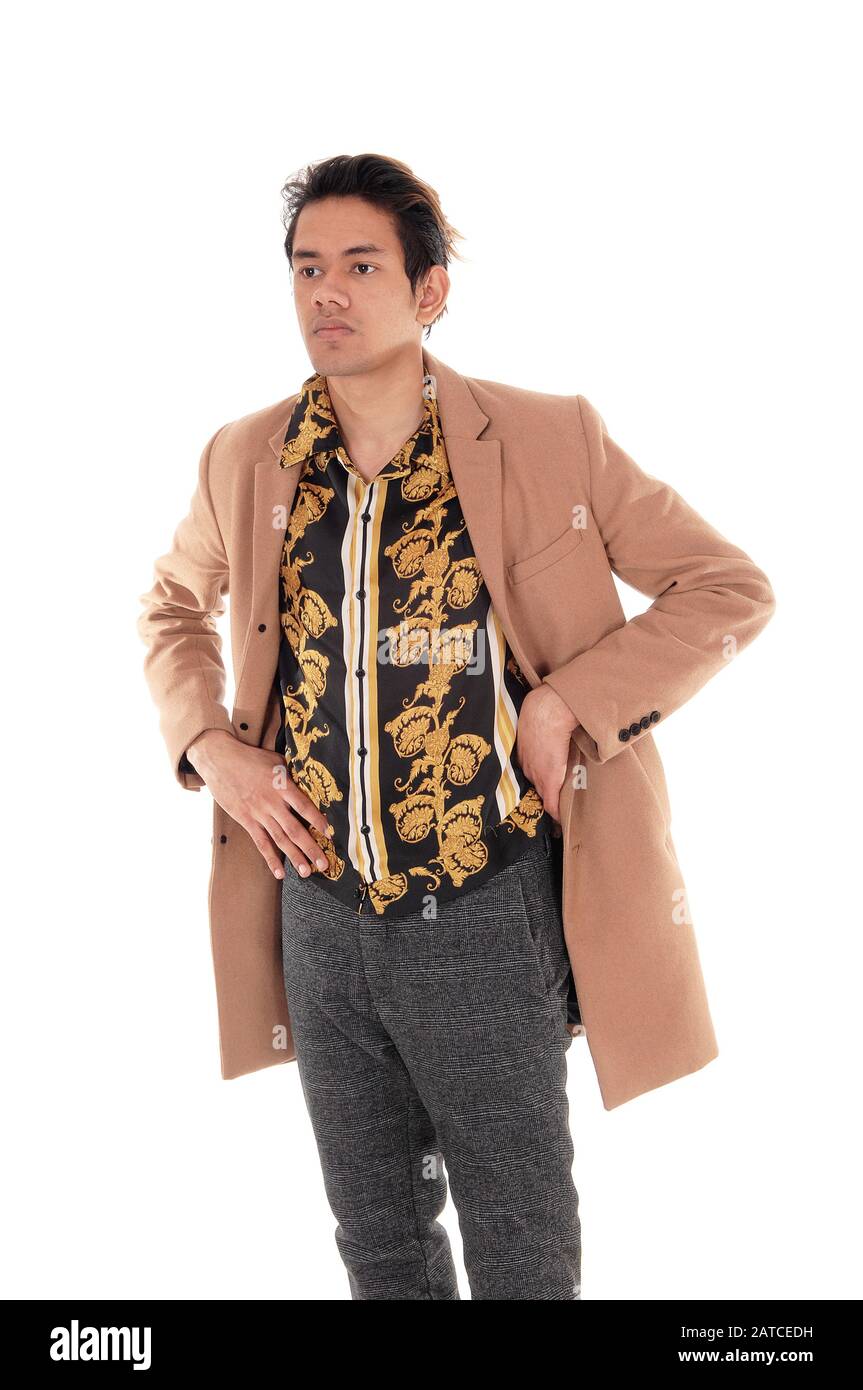 Un bel ragazzo alto che si alza con le mani sui fianchi in un cappotto beige che guarda lontano, isolato per sfondo bianco Foto Stock