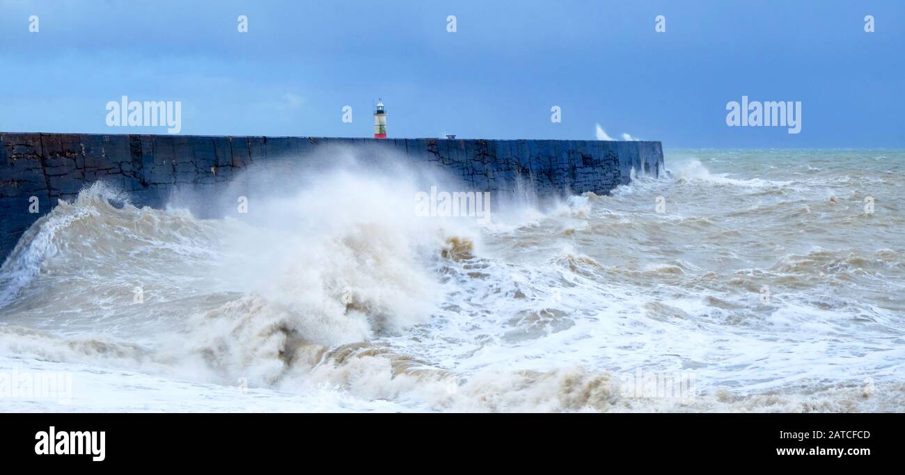 Un muro di porto con un mare tempestoso che si schianta contro il muro causando il mare sfocato e in movimento, dietro c'è un faro rosso e bianco, wav Foto Stock