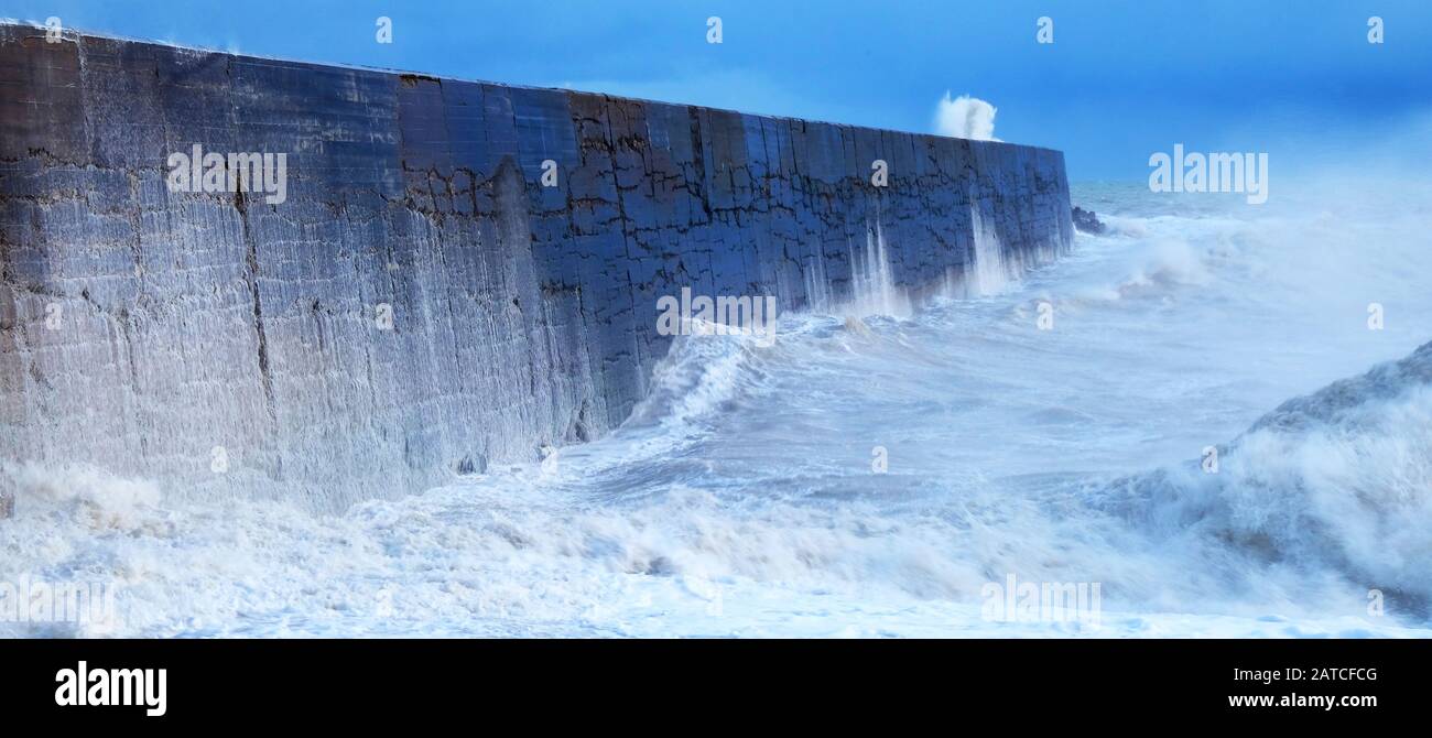 Un muro di porto con un mare tempestoso che si schianta contro il muro causando il mare sfocato e in movimento, le onde si schiantano sopra il muro, lì io Foto Stock