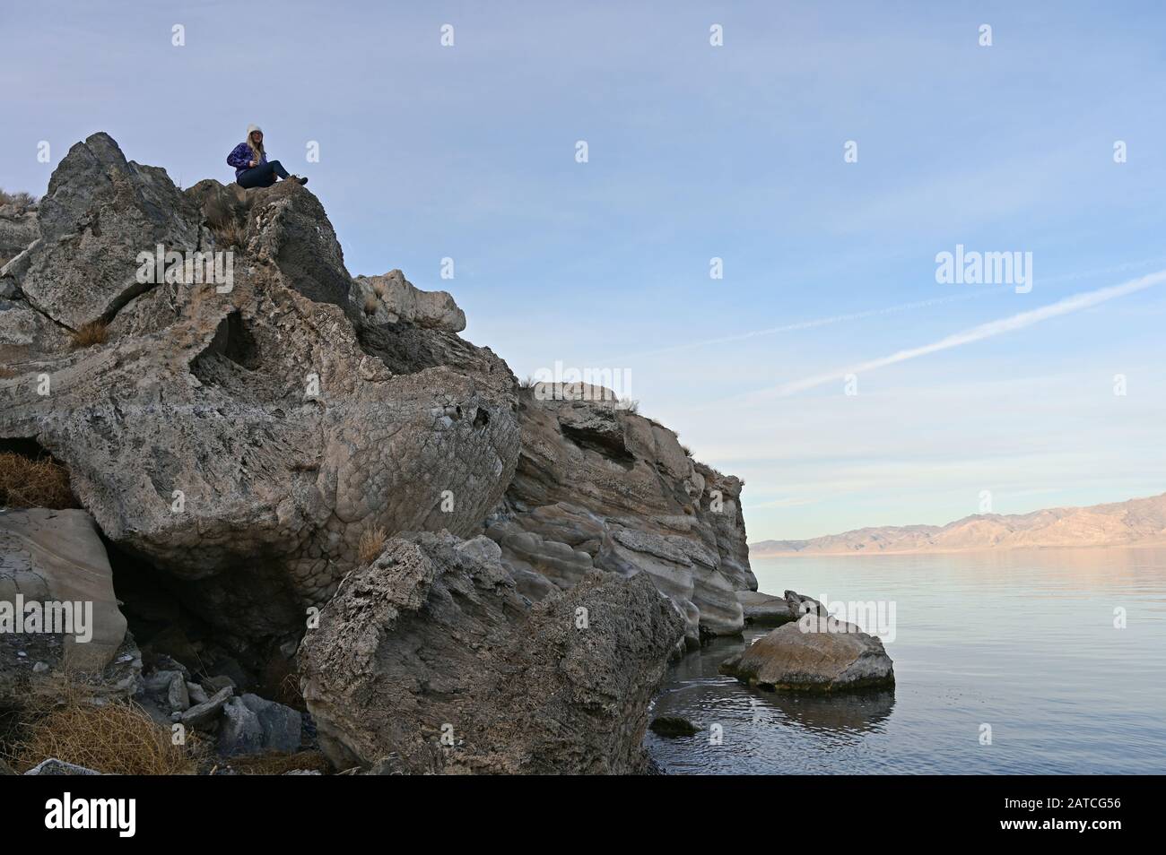 Giovane donna nel maglione blu gode di vista sul tranquillo Lago Piramide, Nevada dalla formazione di roccia sulla costa, in un tranquillo pomeriggio invernale chiaro. Foto Stock