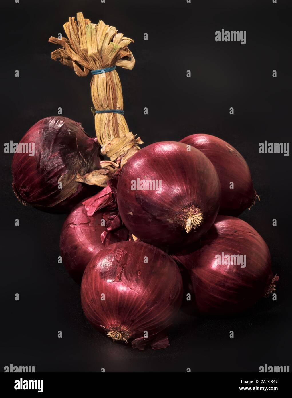 Primo piano di un mazzo di cipolle rosse di Tropea legate su uno sfondo nero Foto Stock