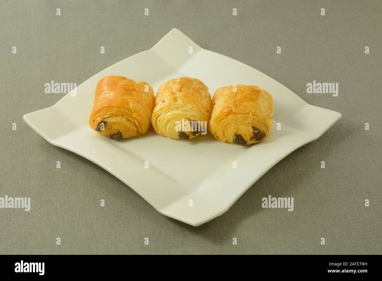 Tre piccole brioche al cioccolato per colazione su un piatto bianco su tovaglia grigia Foto Stock