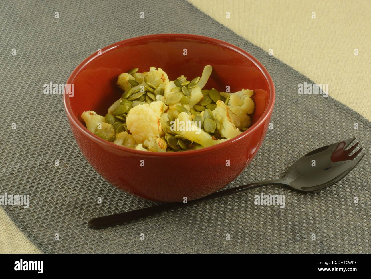 Cavolfiore arrosto con pepitas in ciotola rossa con spork nero sul corridore burlap del tavolo Foto Stock