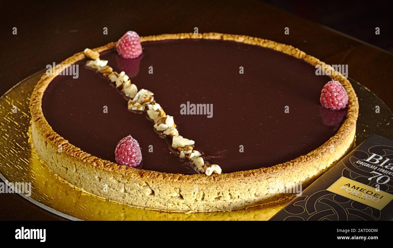 Crostata rotonda con frolla piena di ganache di cioccolato fondente al lampone e decorata con lamponi e noci. Bar di cioccolato Amedei. Foto Stock
