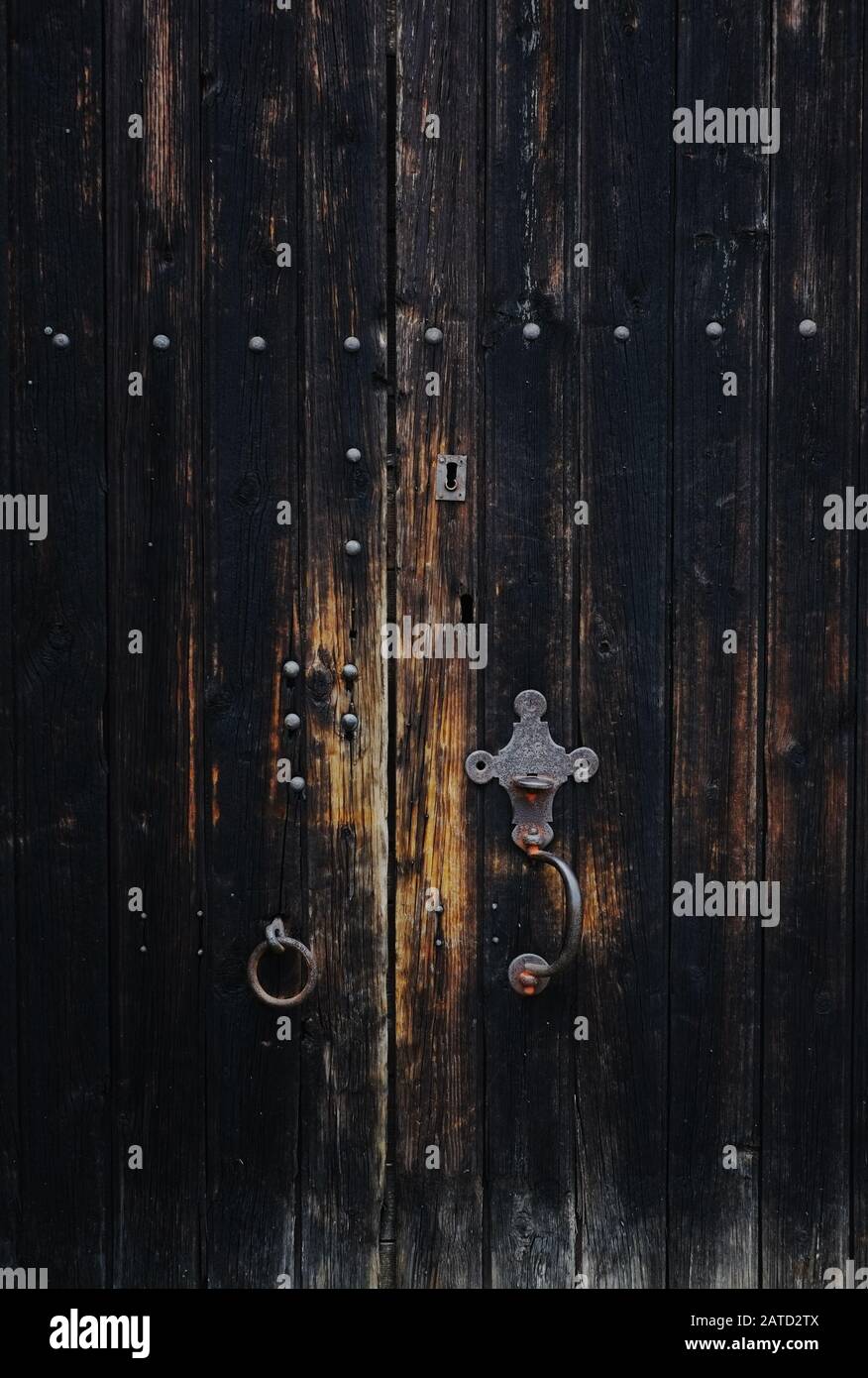 Una vecchia porta in legno slattato annerito con perni in ferro, serratura e maniglia, piastra di taglio in ghisa. Legno biondo indossato vicino alle maniglie, dall'uso. Foto Stock