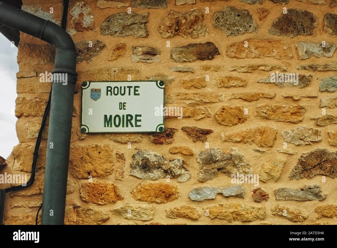 Cartello stradale ROUTE de MOIRE su una casa di pietre dorate accanto alla strada di campagna da Bagnols a Oingt, nella regione vinicola francese di Beaujolais Foto Stock
