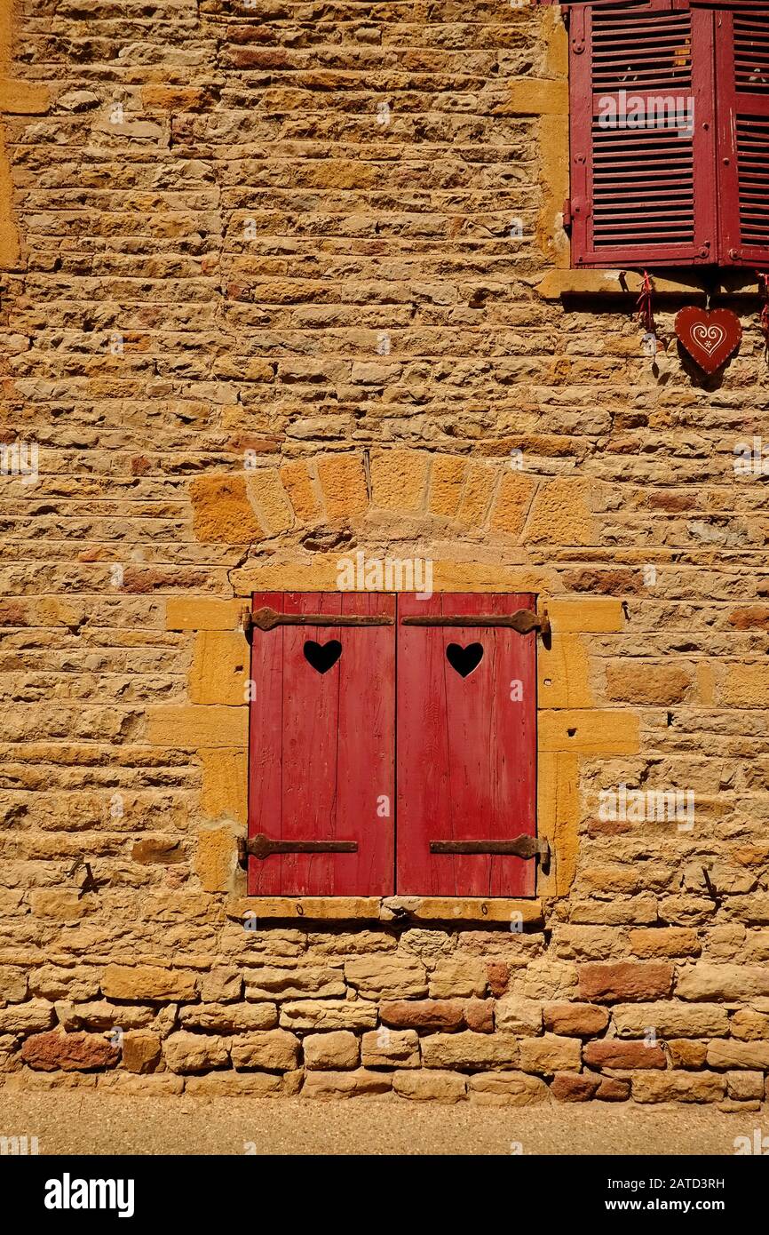 Persiane in legno rosso, dettagli del cuore e le pareti delle case fatte dalle pietre dorate nella bella città medievale di Oingt Francia Foto Stock