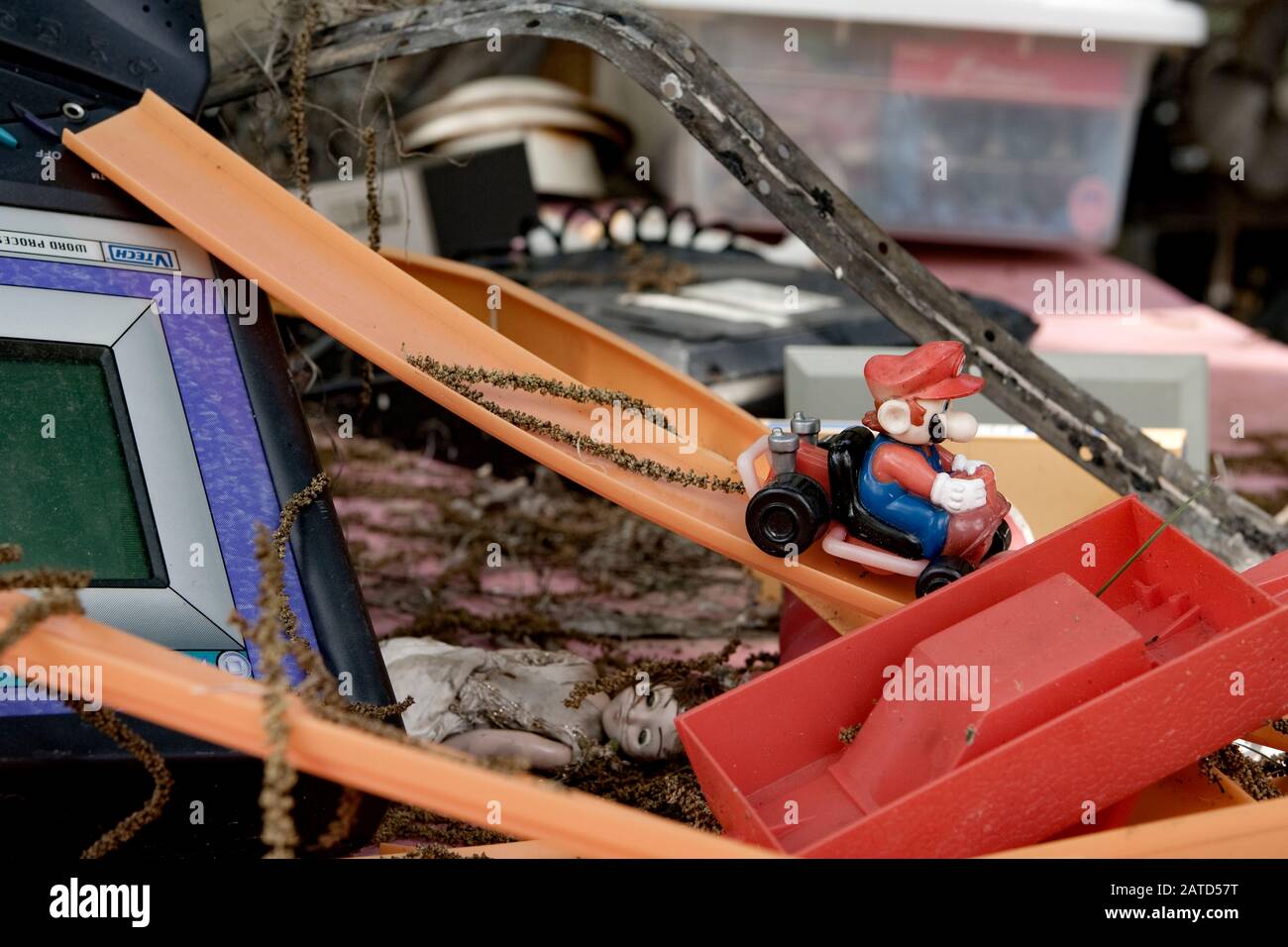 Un giocattolo Mario Kart su una sezione di pista giocattolo Hot Wheels, con una bambola femminile scartata a soffietto, su una panca, dietro un negozio di risparmio. Foto Stock