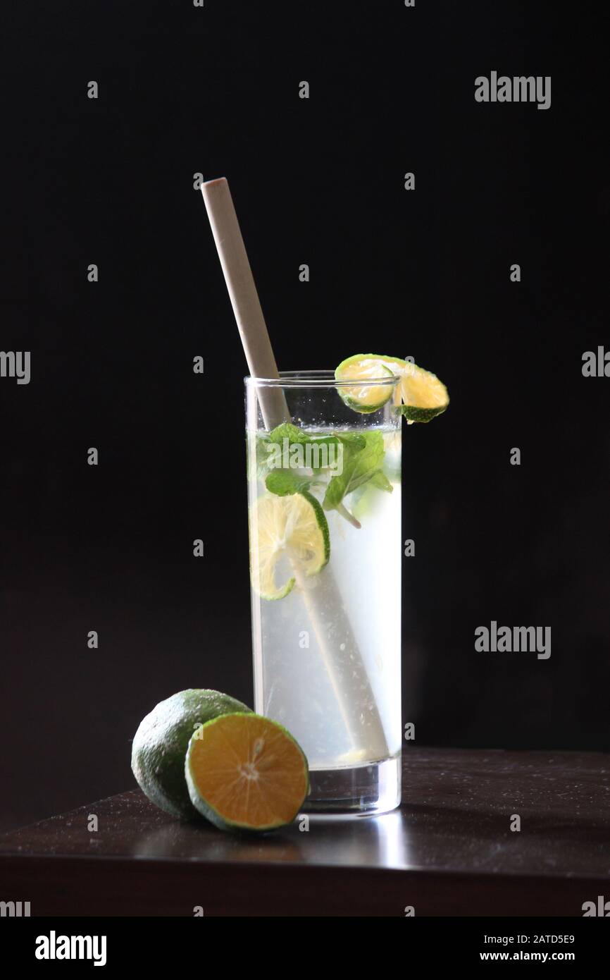 Limonata soda in Tall vetro con cannuccia di bambù con foglie di menta e limoni freschi tagliati sullo sfondo Foto Stock