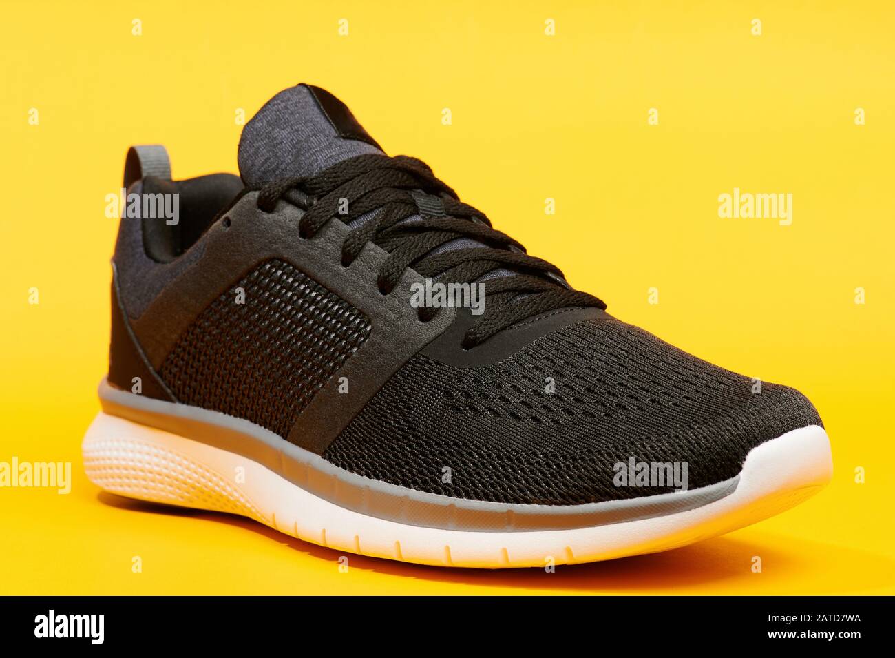 Una scarpa da running nera su sfondo giallo, vista ravvicinata Foto Stock