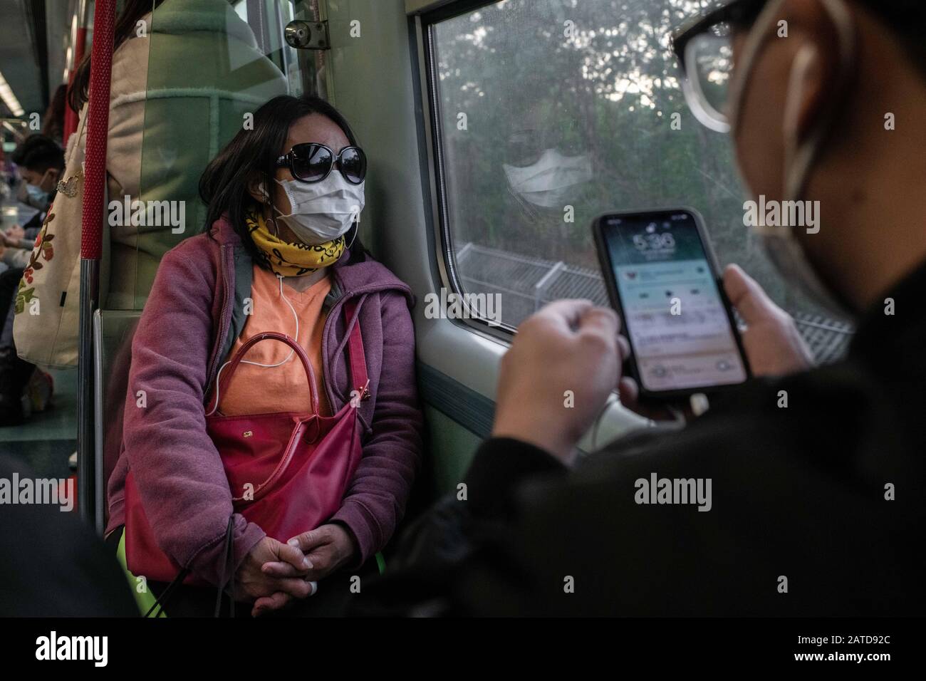 Una donna indossa occhiali da sole e maschere chirurgiche in un treno MTR in direzione di lo Wu al confine con Shenzhen.The Organizzazione Mondiale della Sanità ha chiamato un'emergenza sanitaria globale, invertendo la decisione precedente su focolaio di coronavirus. Finora ci sono 13 casi confermati di coronavirus a Hong Kong, mentre il totale dei casi confermati è salito a 14.549 e il numero dei decessi è salito a 305. Foto Stock