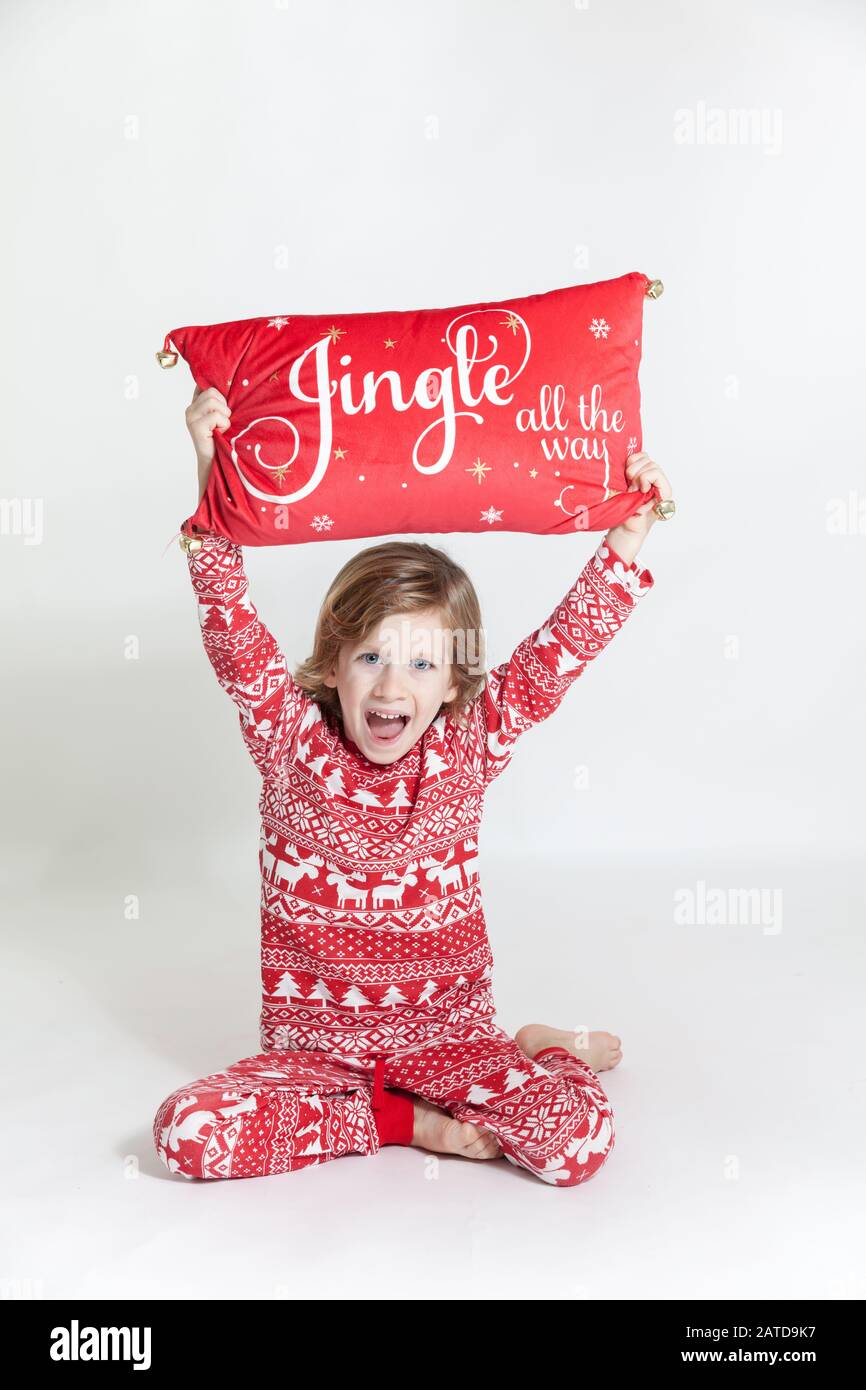 Ritratto di un ragazzo felice in pigiami che tiene un cuscino di Natale sopra la testa Foto Stock