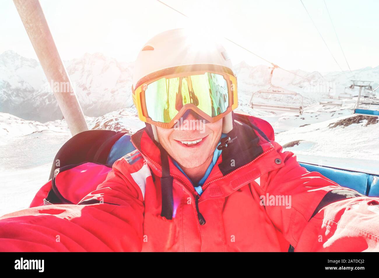 Felice sciatore scattare foto selfie con fotocamera smartphone seduta su skilift - giovane uomo divertirsi in inverno vacanza neve resort con luce posteriore - Spo Foto Stock