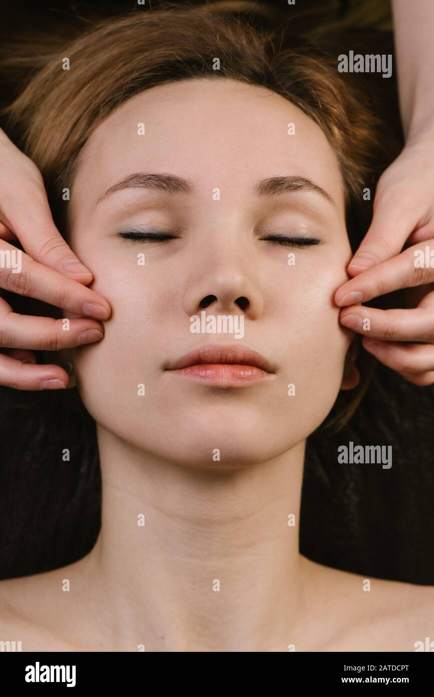 Mani massaggiando le guance della donna con le dita alla clinica asiatica di bellezza. Vista dall'alto Foto Stock