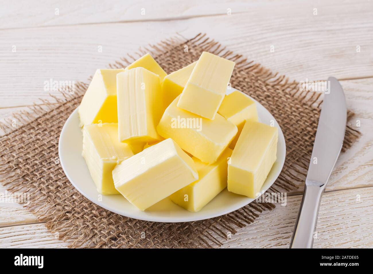 Pezzi rettangolari di burro giallo fresco su un piattino bianco e coltello da tavola sopra un tavolo di legno bianco. Latticini. Burro sandwich. Nutriente grasso naturale. Foto Stock